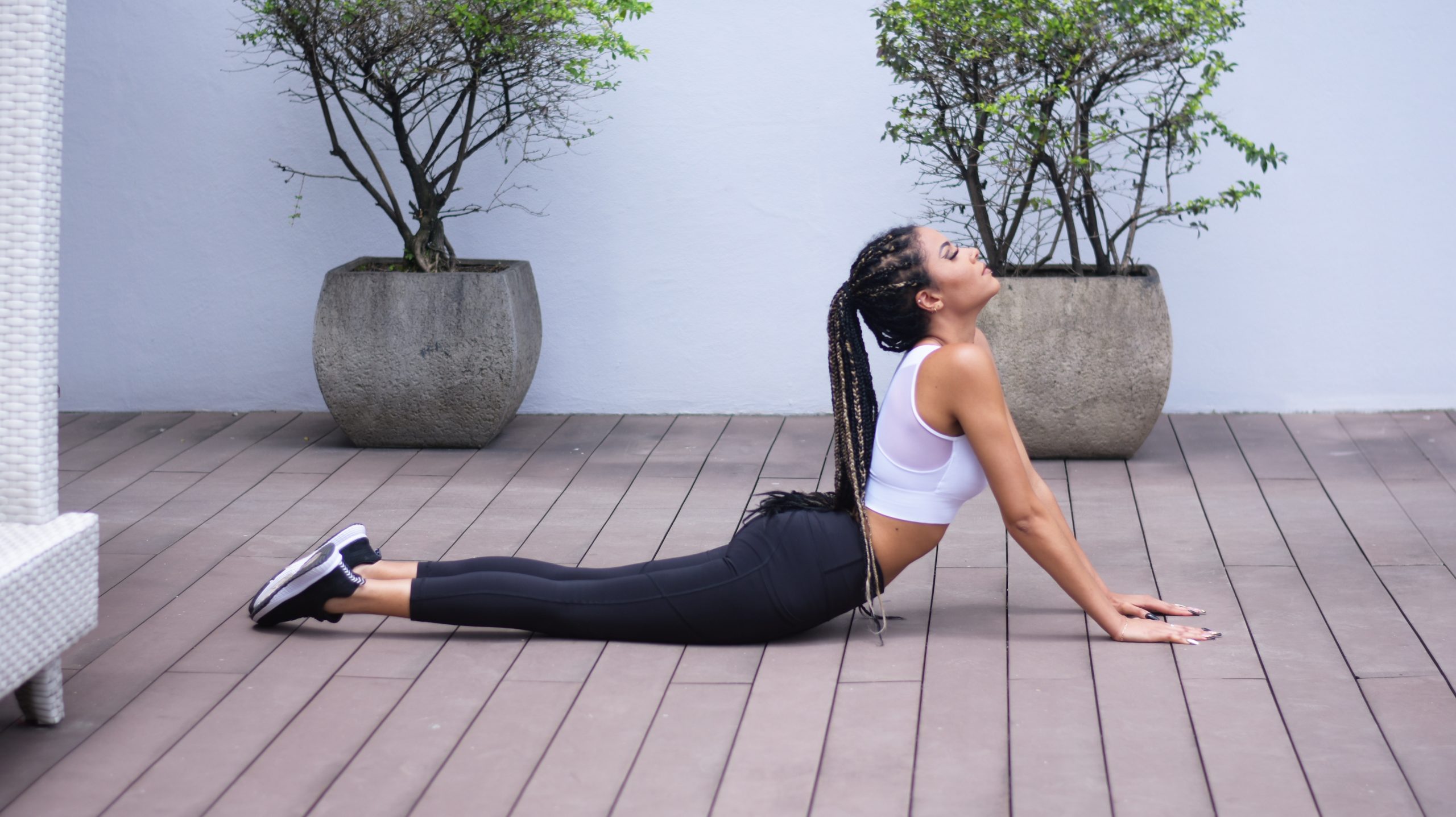 A toned woman stretching in a cobra pose on an outdoor bright wooden decking